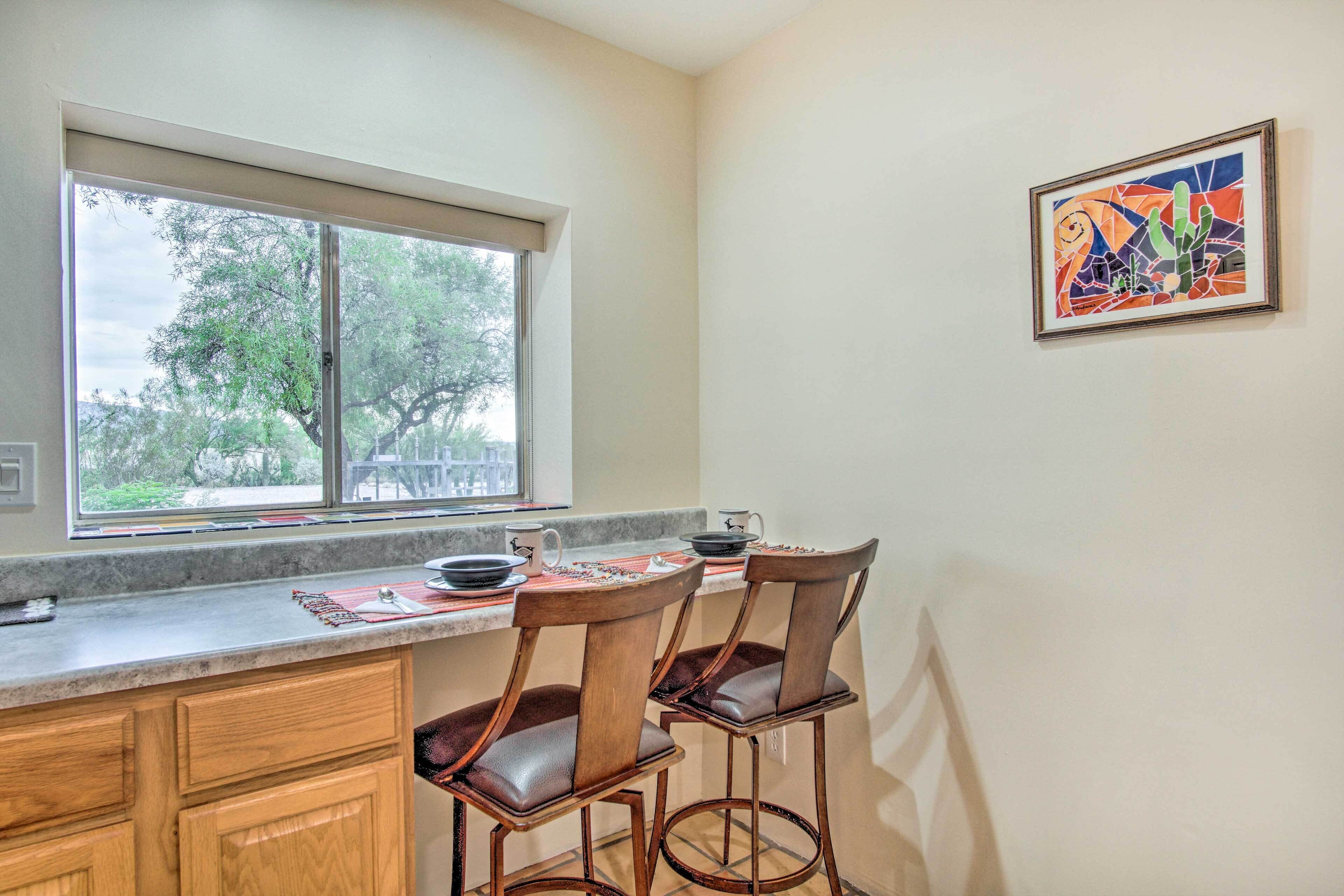 A kitchen with a window, two wooden bar stools, and a framed artwork on the wall.