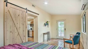 A bedroom with a bed, a sliding door, a chair, a table, and a view of the kitchen.