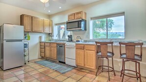 A kitchen with wooden cabinets, a stainless steel refrigerator, a microwave, a dishwasher, and a stove. There are two bar stools and a window providing a view outside.