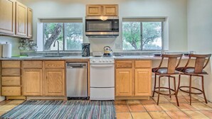 A kitchen with wooden cabinets, a microwave, a stove, and a dishwasher. There are two windows and a rug on the floor.