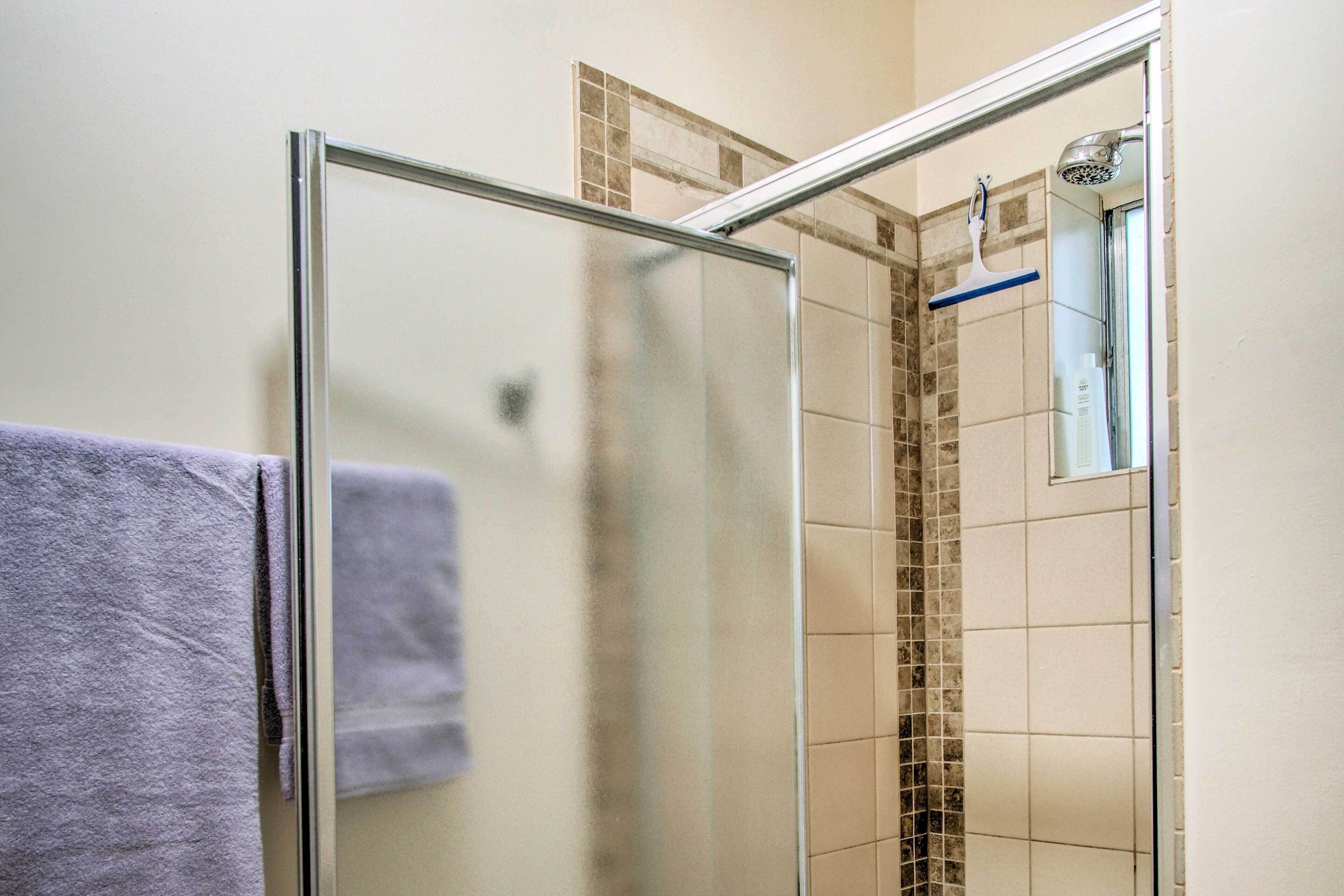 Une douche fermée par des parois en verre, dotée d’un pommeau de douche et d’un porte-serviettes bleu.