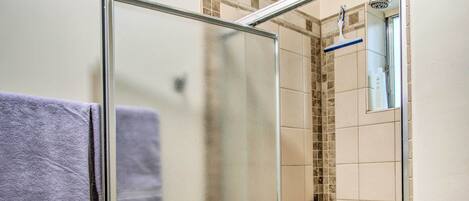 Une douche fermée par des parois en verre, dotée d’un pommeau de douche et d’un porte-serviettes bleu.