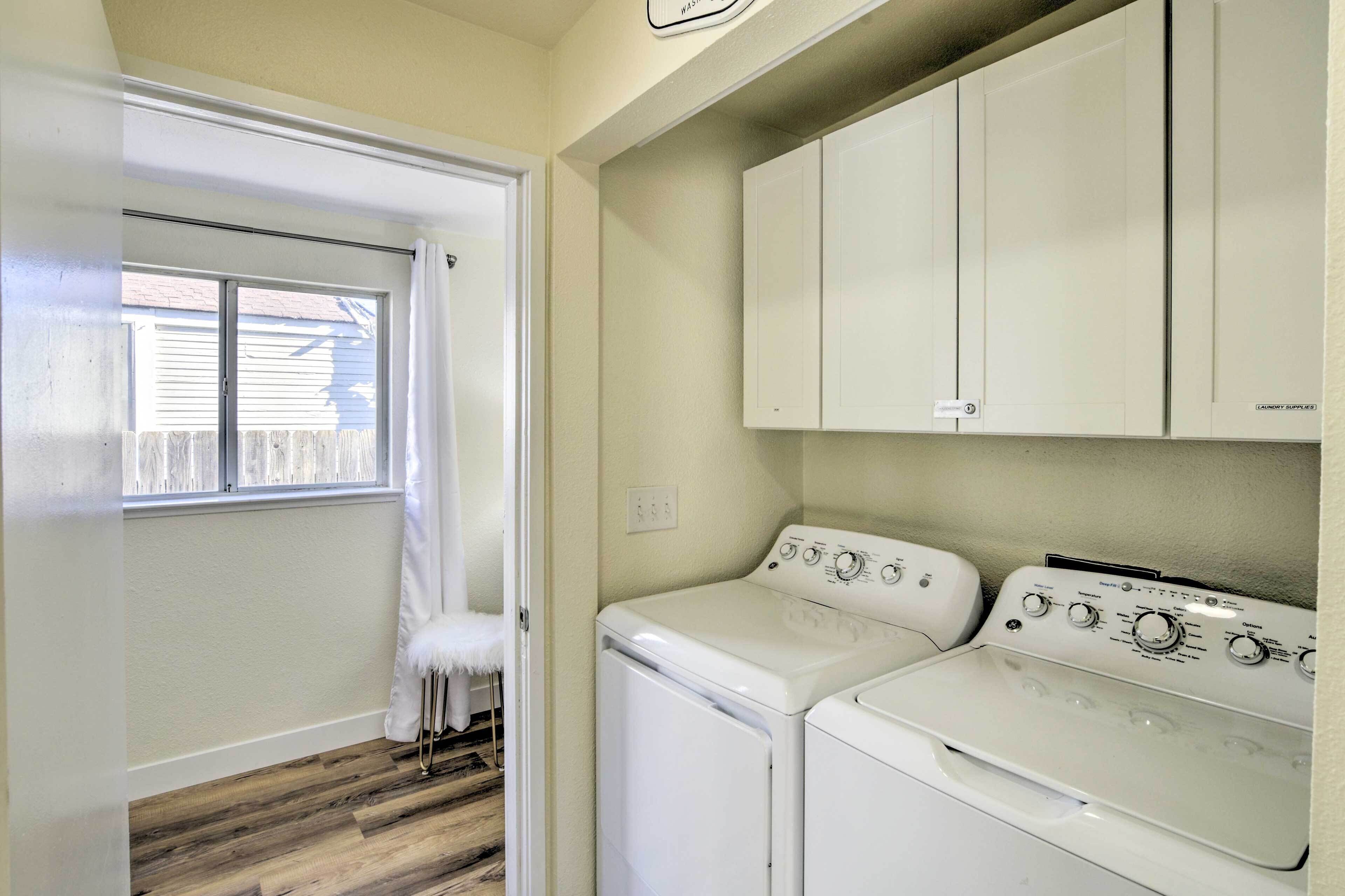 A laundry room with a washer and dryer, wooden flooring, and a window with curtains.