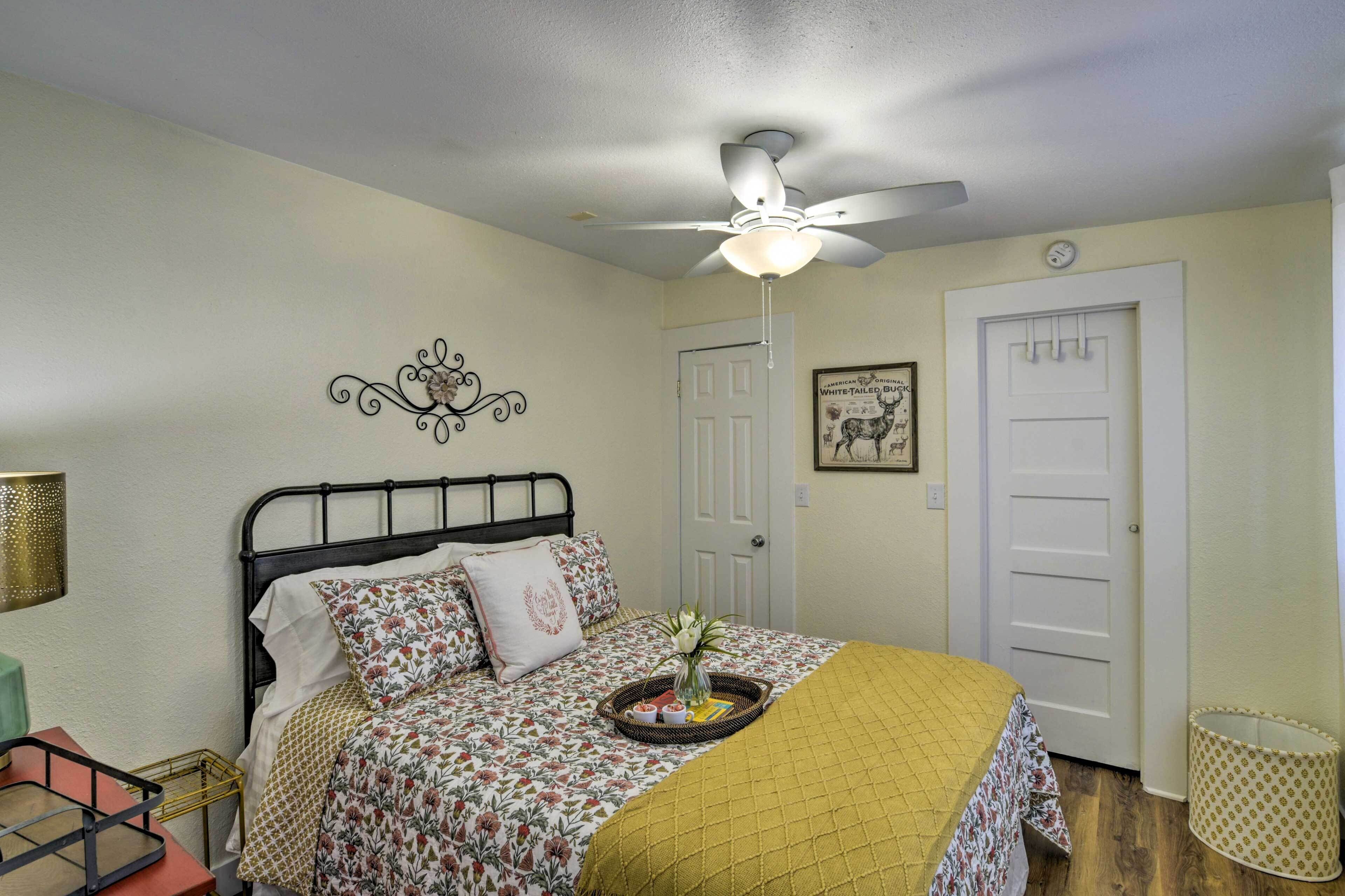 A bedroom with a bed, a ceiling fan, a door, and a wall decoration.