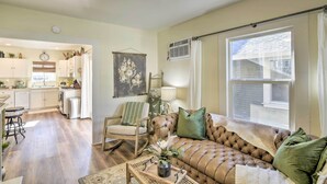 A spacious living room with a large window, a sofa, a chair, and a kitchen area in the background. - Centrally Located House in Chico w/ Gas Grill (Chico)