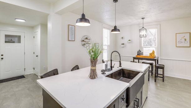 Een moderne keuken met een centraal kookeiland, hanglampen, en een eethoek met een kleine tafel en stoelen.