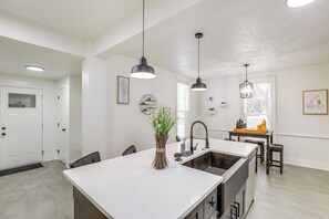 Eine moderne Küche mit einer zentralen Kochinsel, Pendelleuchten und einem Essbereich mit einem kleinen Tisch und Stühlen.
