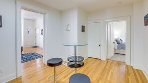 Een hal met houten vloer, een glazen tafel met een zwarte stoel, en een deur die leidt naar een slaapkamer.
