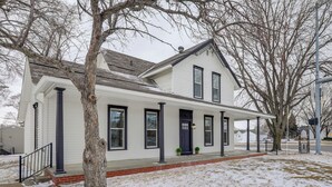 Een tweelaags huis met een overdekte veranda, een fundering van baksteen en een met sneeuw bedekte gazon.