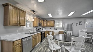 A modern kitchen with wooden cabinets, stainless steel appliances, a marble countertop, and a dining area with white chairs.