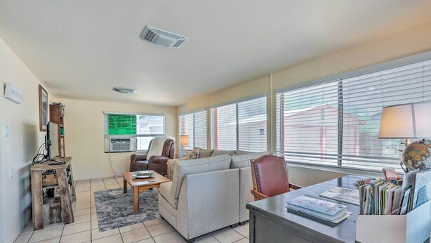 A living room with a sofa, a coffee table, a desk with a lamp, and a bookshelf. - Adobe-style Tumacacori Home w/ Trail Access! (Tumacacori)