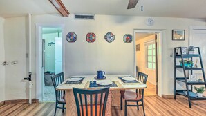 A dining area with a wooden table set for four, surrounded by chairs, and a black shelf with plants to the right. - Adobe-style Tumacacori Home w/ Trail Access! (Tumacacori)