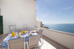 A dining table with a blue and white tablecloth, set with plates, a pitcher of orange juice, and a bowl of fruit. - Casa Darly in Positano (Positano)