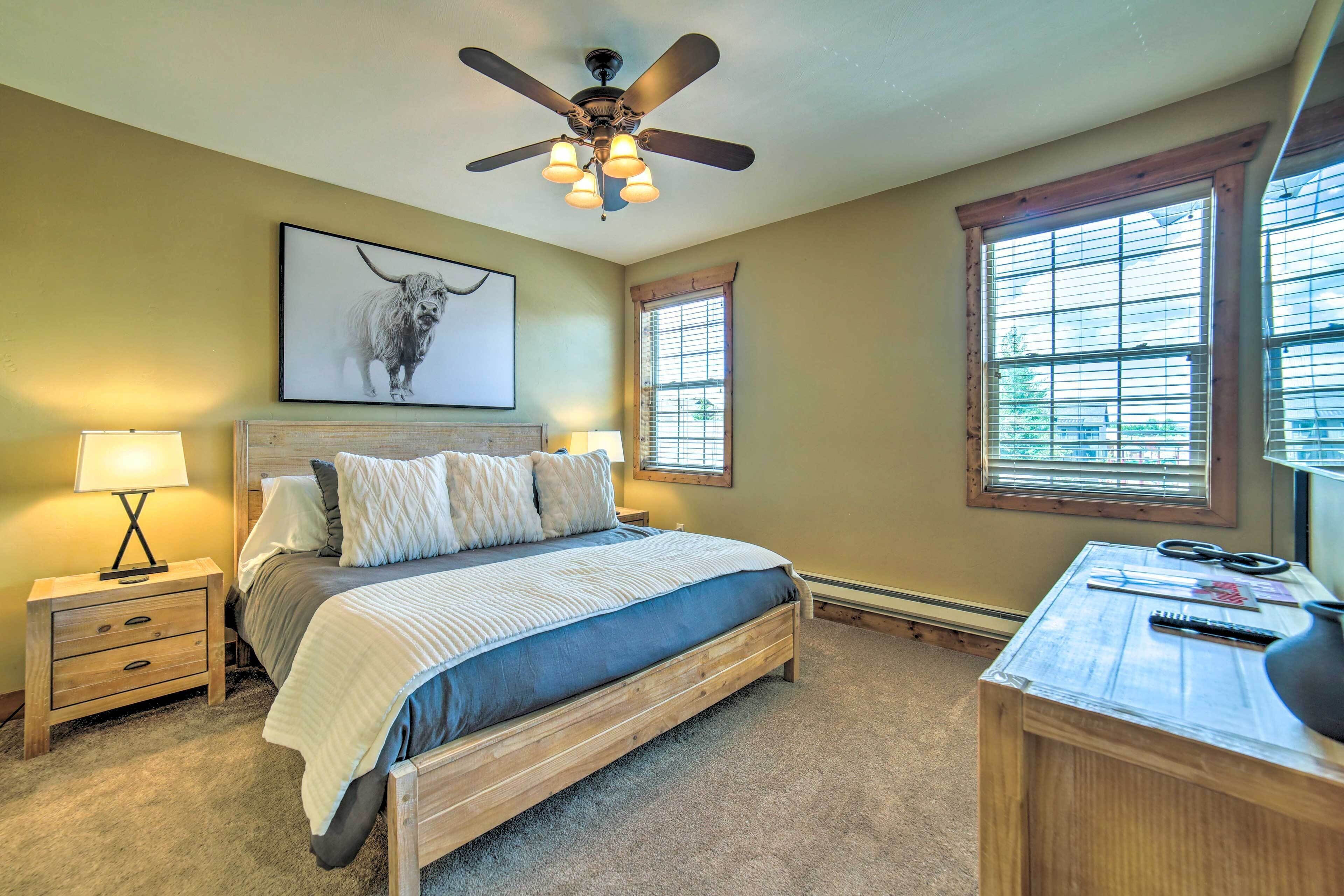 A bedroom with a bed, a desk, a ceiling fan, and two windows.