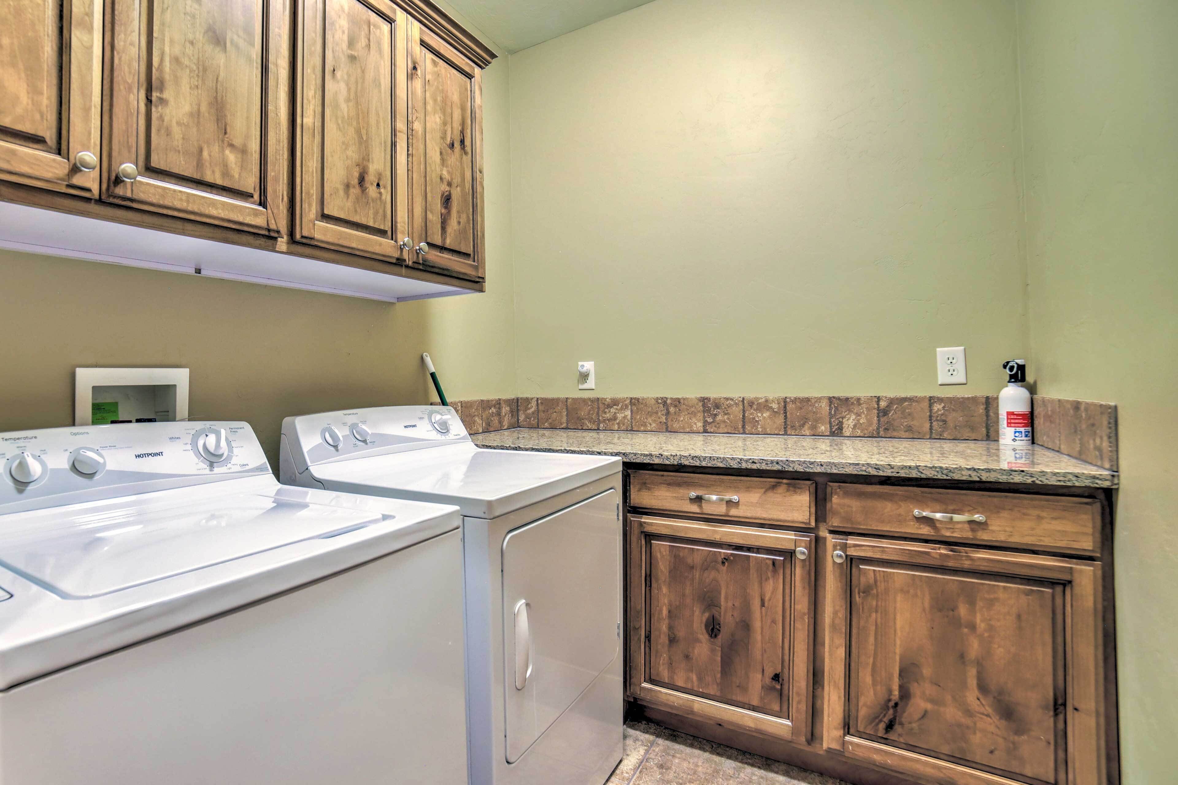 A laundry area with two white washing machines, wooden cabinets, a granite countertop, and a fire extinguisher.