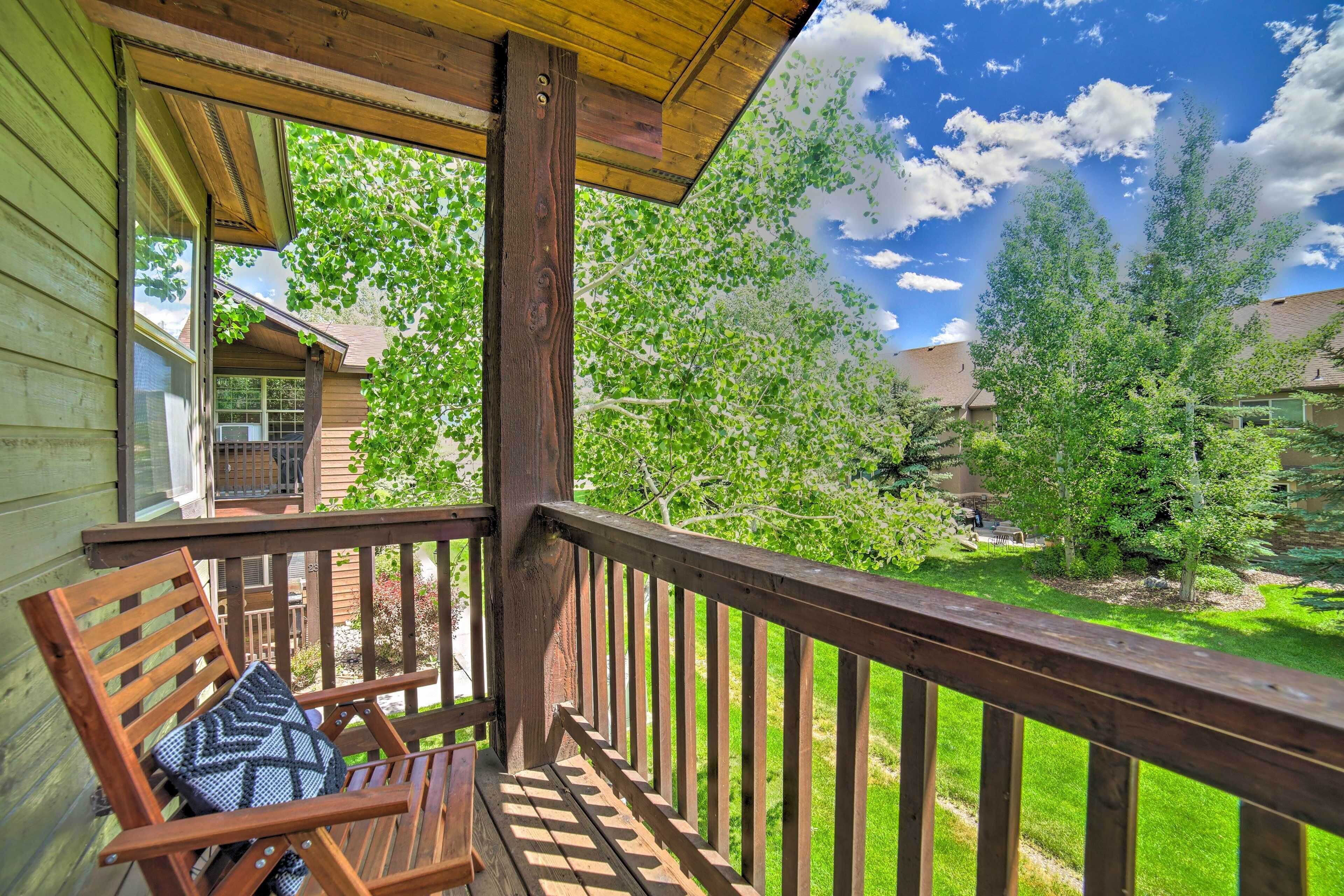 A wooden deck with a wooden chair and a cushion, overlooking a well-maintained lawn and trees.