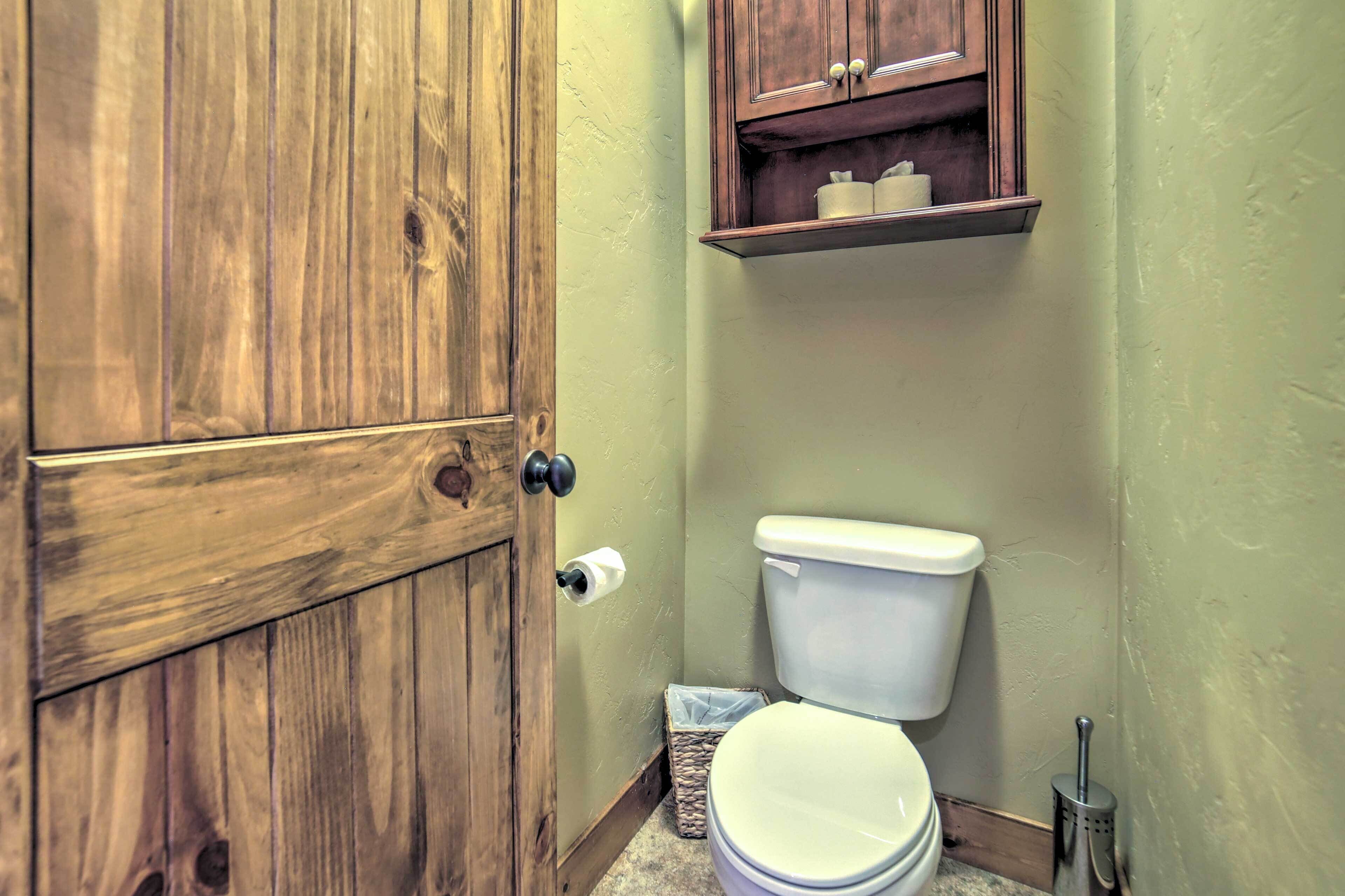 Un baño con puerta de madera, inodoro, estante sobre el inodoro y un cubo de basura.
