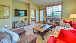 A living room with a brown leather sofa, a red sofa, a wooden coffee table, and a television mounted on the wall. - Cozy Driggs Condo ~ 40 Mi to Grand Teton NP! (Driggs)