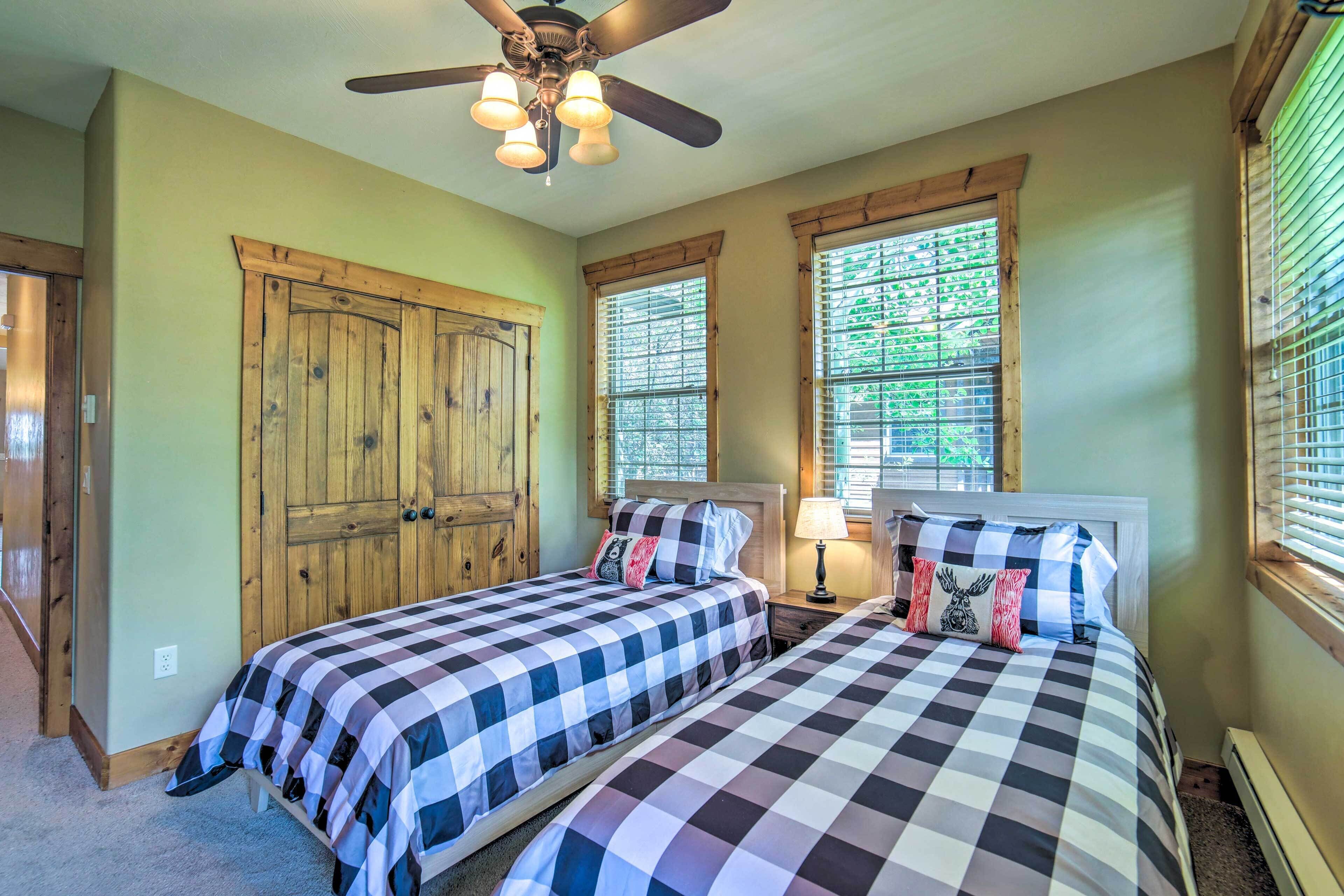 A bedroom with two beds, a ceiling fan, and large windows with blinds.