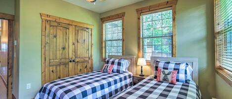 A bedroom with two beds, a ceiling fan, and large windows with blinds.