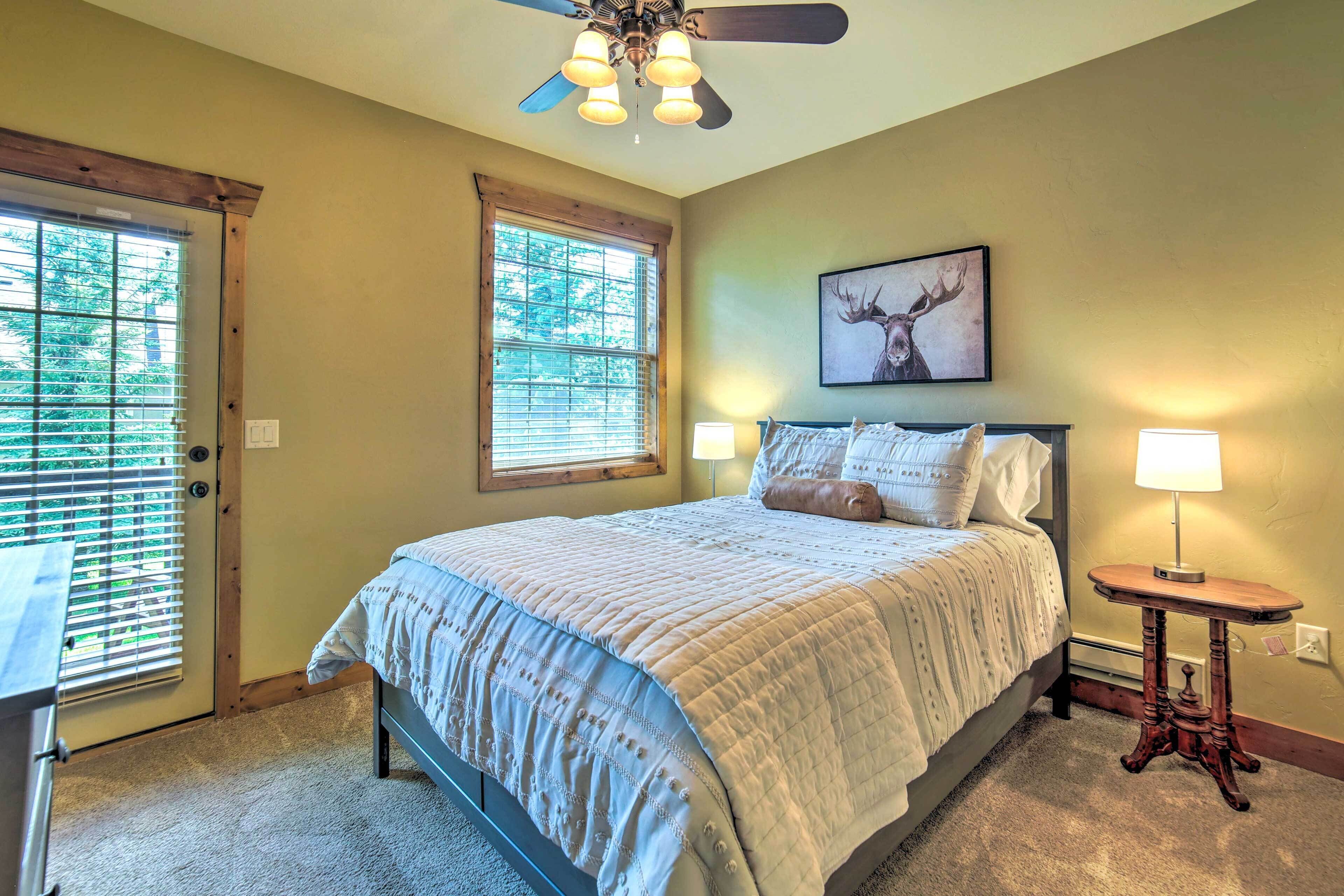 A bedroom with a bed, two bedside lamps, a ceiling fan, a window with blinds, and a framed deer picture on the wall.