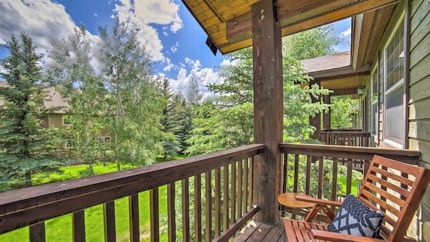 A wooden deck with a wooden chair and a small table, overlooking a green landscape with trees and a house in the background. - Cozy Driggs Condo ~ 40 Mi to Grand Teton NP! (Driggs)