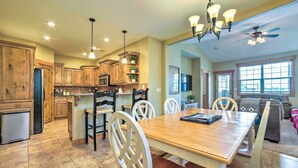 A spacious kitchen with wooden cabinets, a dining area with a wooden table and white chairs, and a ceiling fan. - Cozy Driggs Condo ~ 40 Mi to Grand Teton NP! (Driggs)