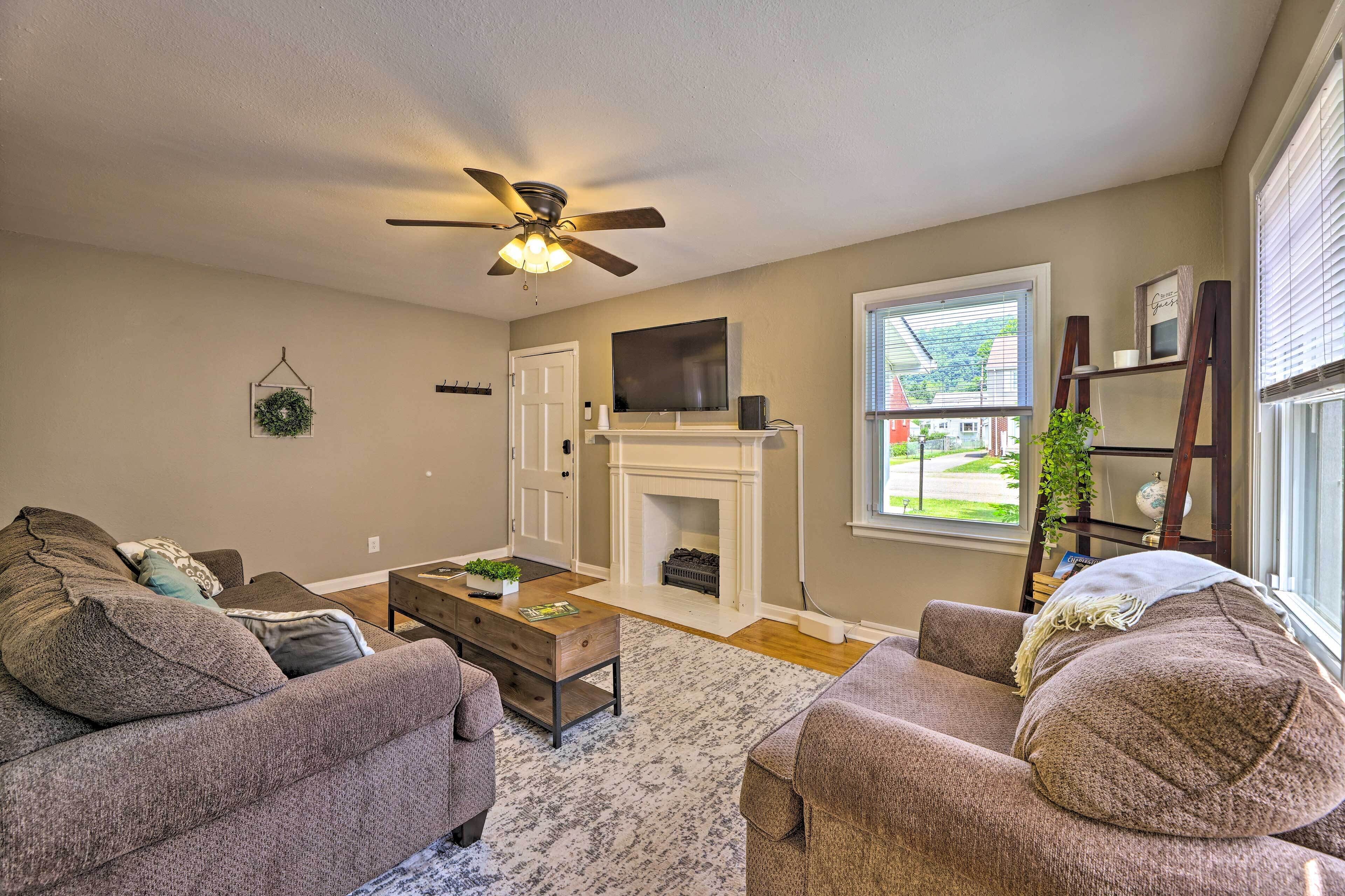A living room with a fireplace, a ceiling fan, and a television on the wall.