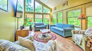 Ein geräumiges Wohnzimmer mit großen Fenstern, einem Deckenventilator und verschiedenen Sitzgelegenheiten, darunter eine Couch, Sessel und ein Couchtisch.