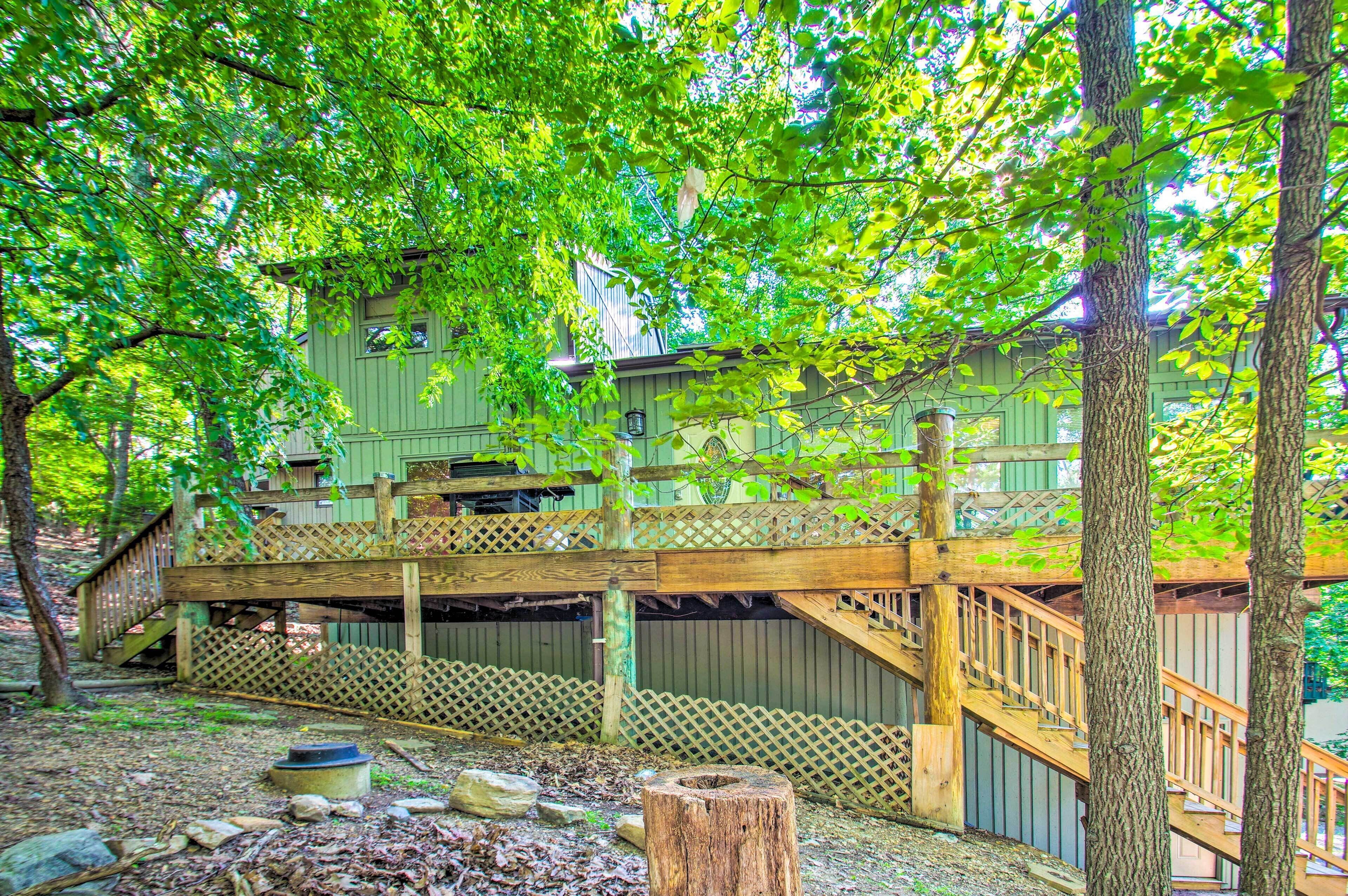 A wooden deck with a staircase leading to a green building surrounded by trees.