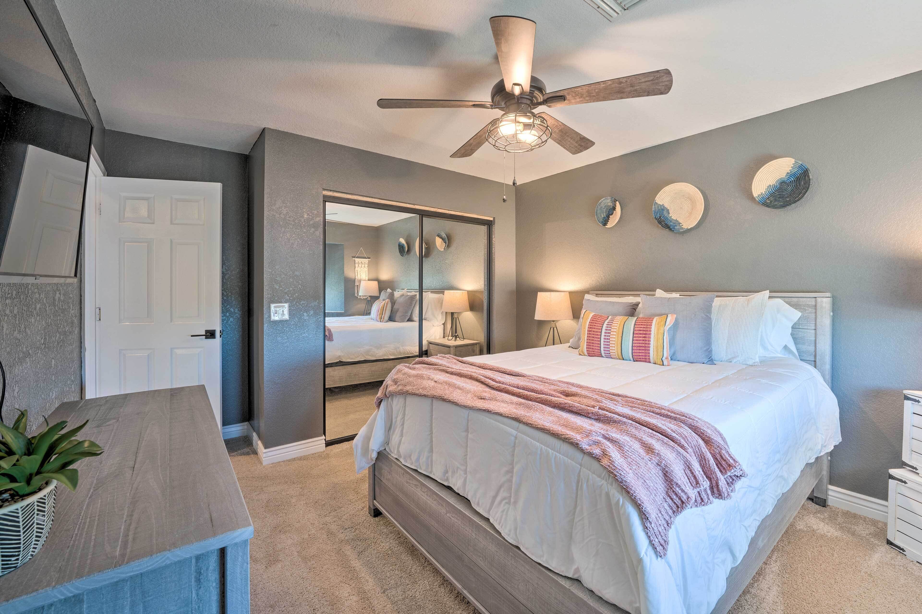 A bedroom with a bed, bedside tables, a ceiling fan, a mirror, and a door.