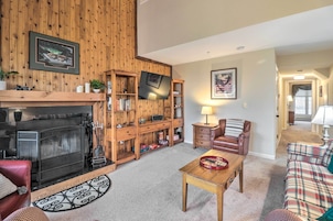 A cozy living room with a fireplace, wooden shelves, a TV, and a plaid sofa.