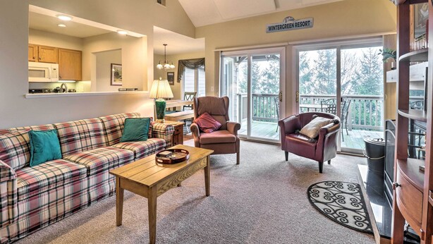 Ett vardagsrum med en soffa i rutigt tyg, ett soffbord i trä och en stol. Ovanför dörren hänger en skylt med texten ”Wintergreen Resort”.