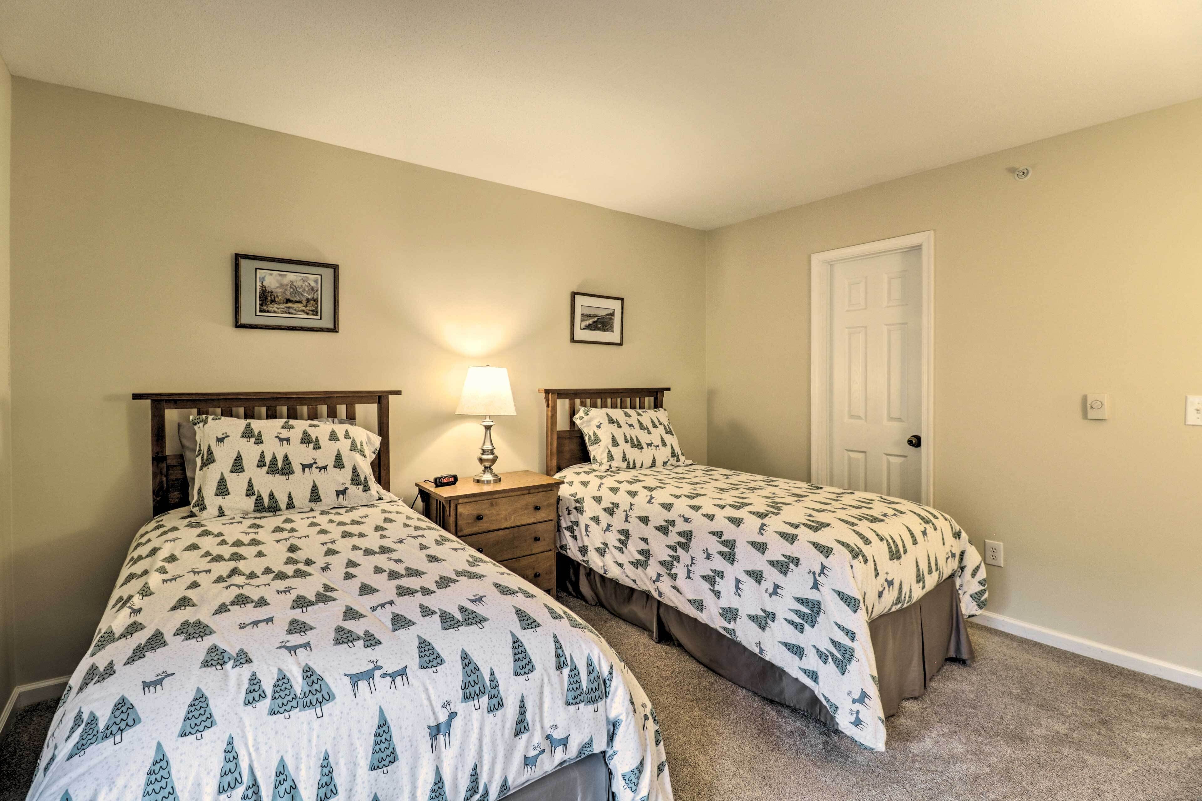 Une chambre avec deux lits, chacun recouvert d’une couvre-lit à motifs, une table de chevet avec une lampe et une porte.