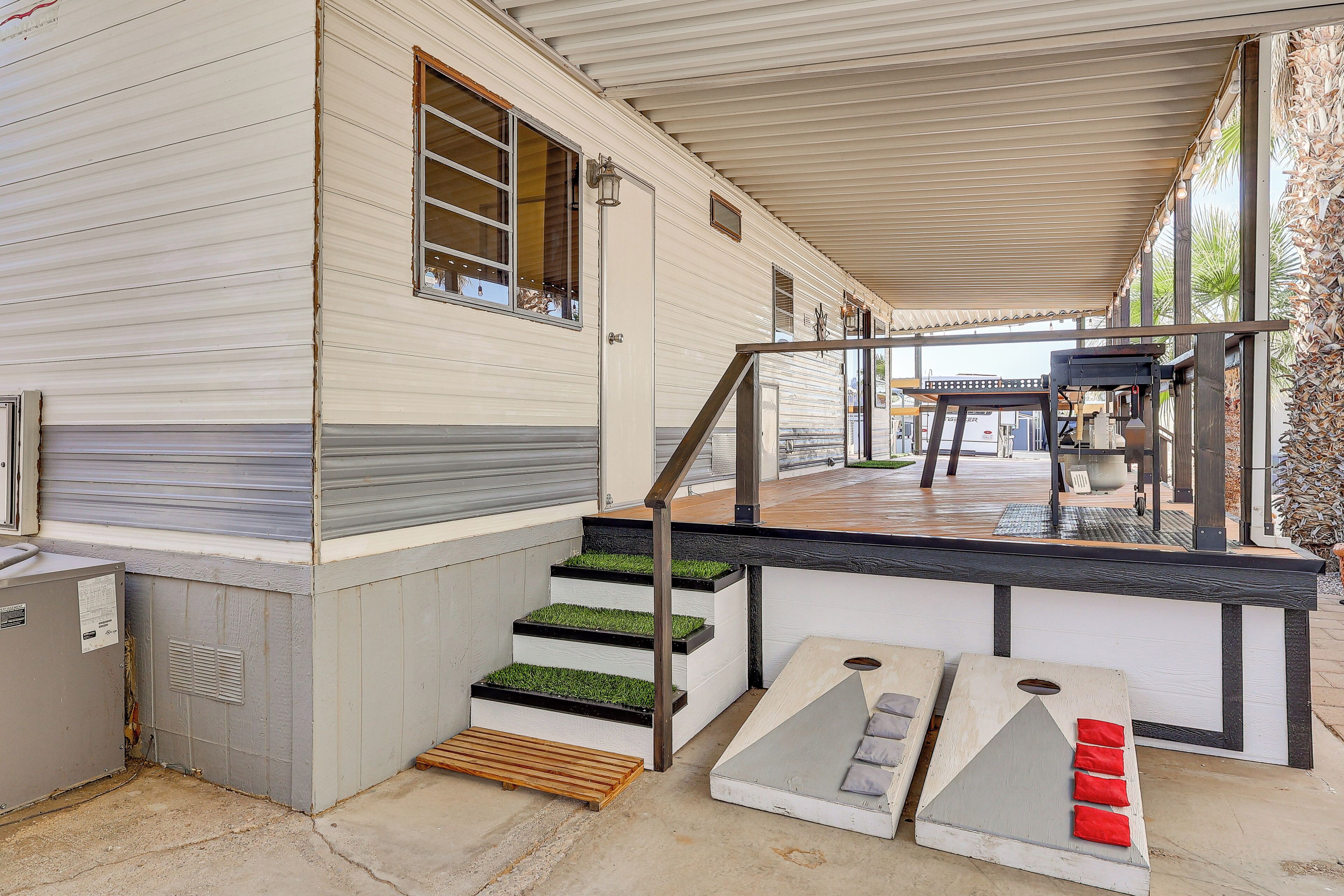 Une maison mobile dotée d’un porche couvert, d’un escalier dont les marches sont recouvertes de gazon artificiel vert, et d’un petit espace de détente extérieur.