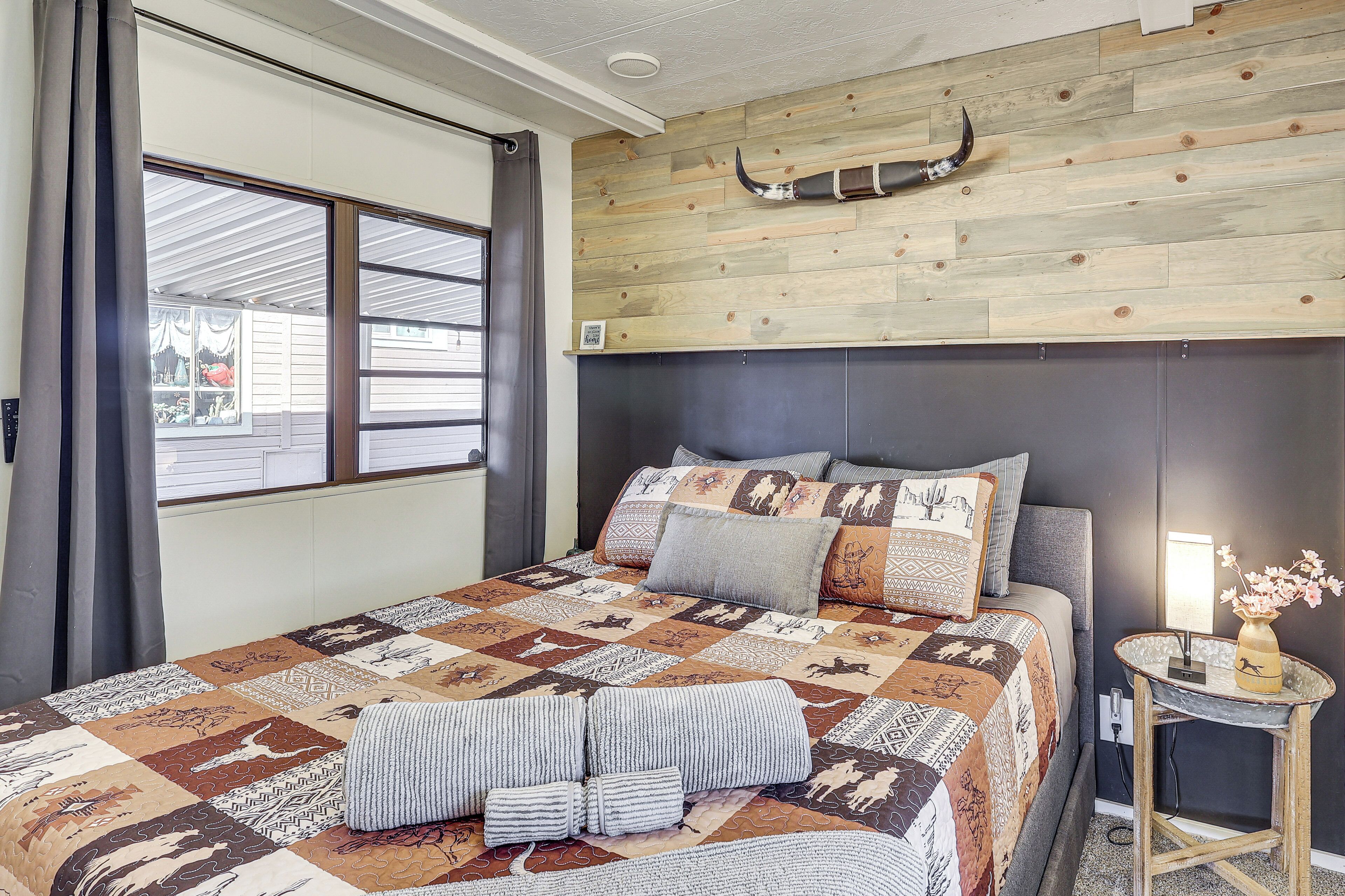 A bedroom with a large bed, a wooden headboard, a small table with a vase, and a window with curtains.