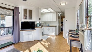 A modern kitchen with white cabinetry, a built-in TV, and a dining area with a wooden table and chairs.