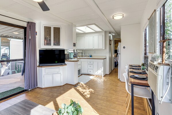 Una cucina moderna con mobili bianchi, una TV integrata e un'area pranzo con tavolo e sedie in legno.