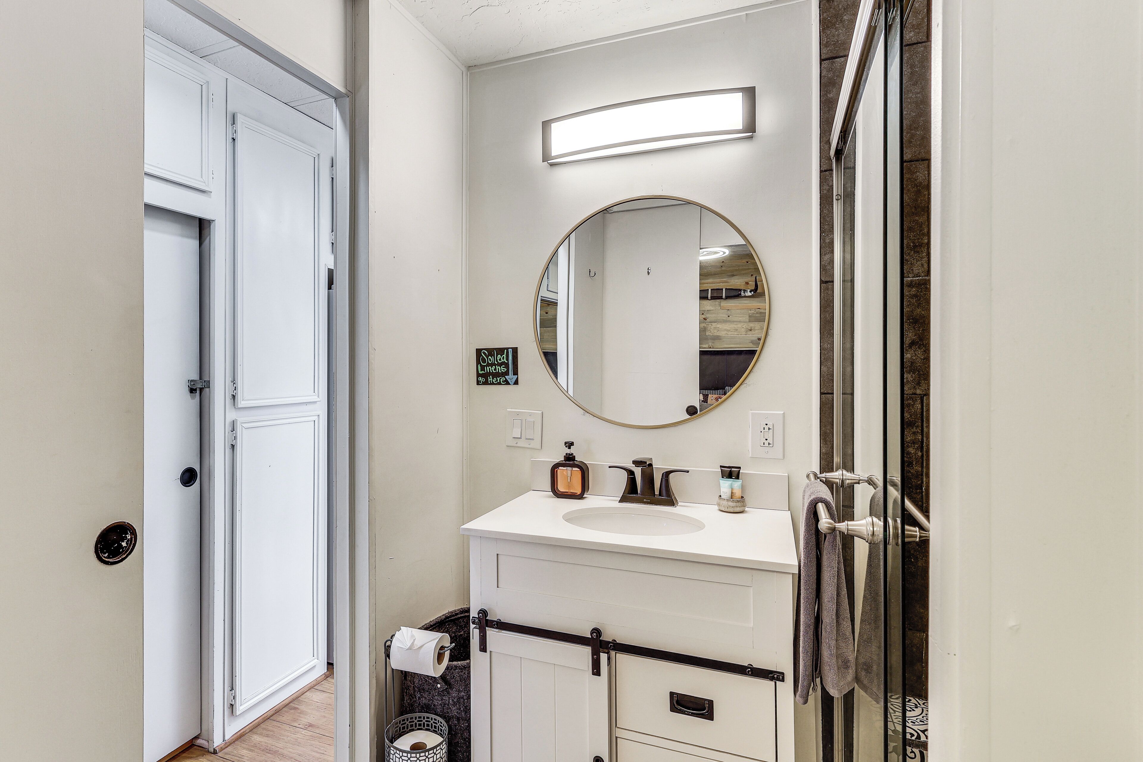 Un bagno con lavandino bianco, uno specchio rotondo, un portascopevoli e una zona doccia.