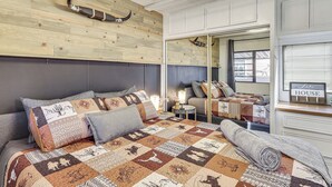 A bedroom with a wooden headboard, a quilted bedspread, a mirror, and a bedside table with a lamp.