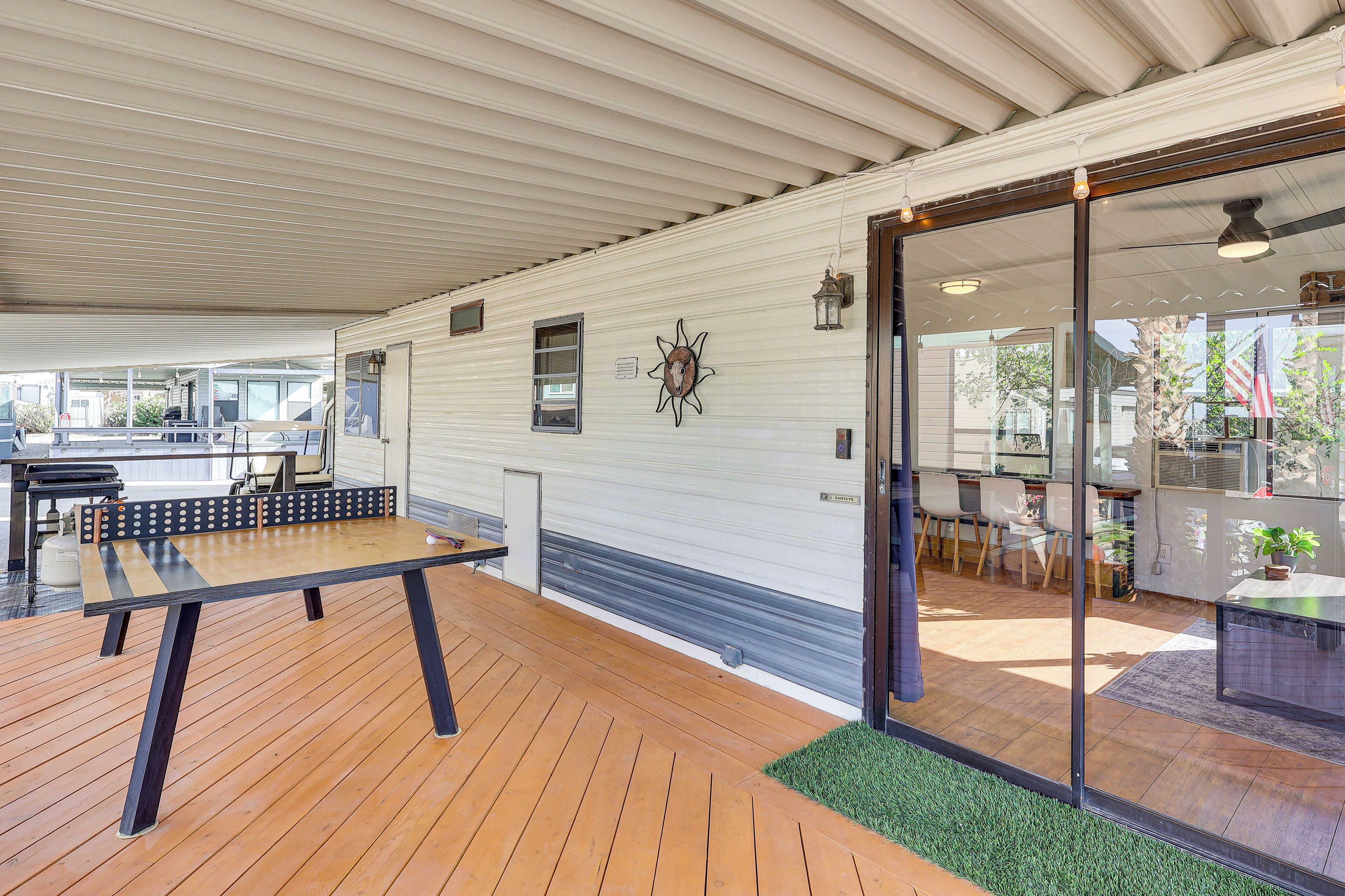 A spacious indoor area with a wooden deck, a dining table, and a glass door leading to a kitchen area.