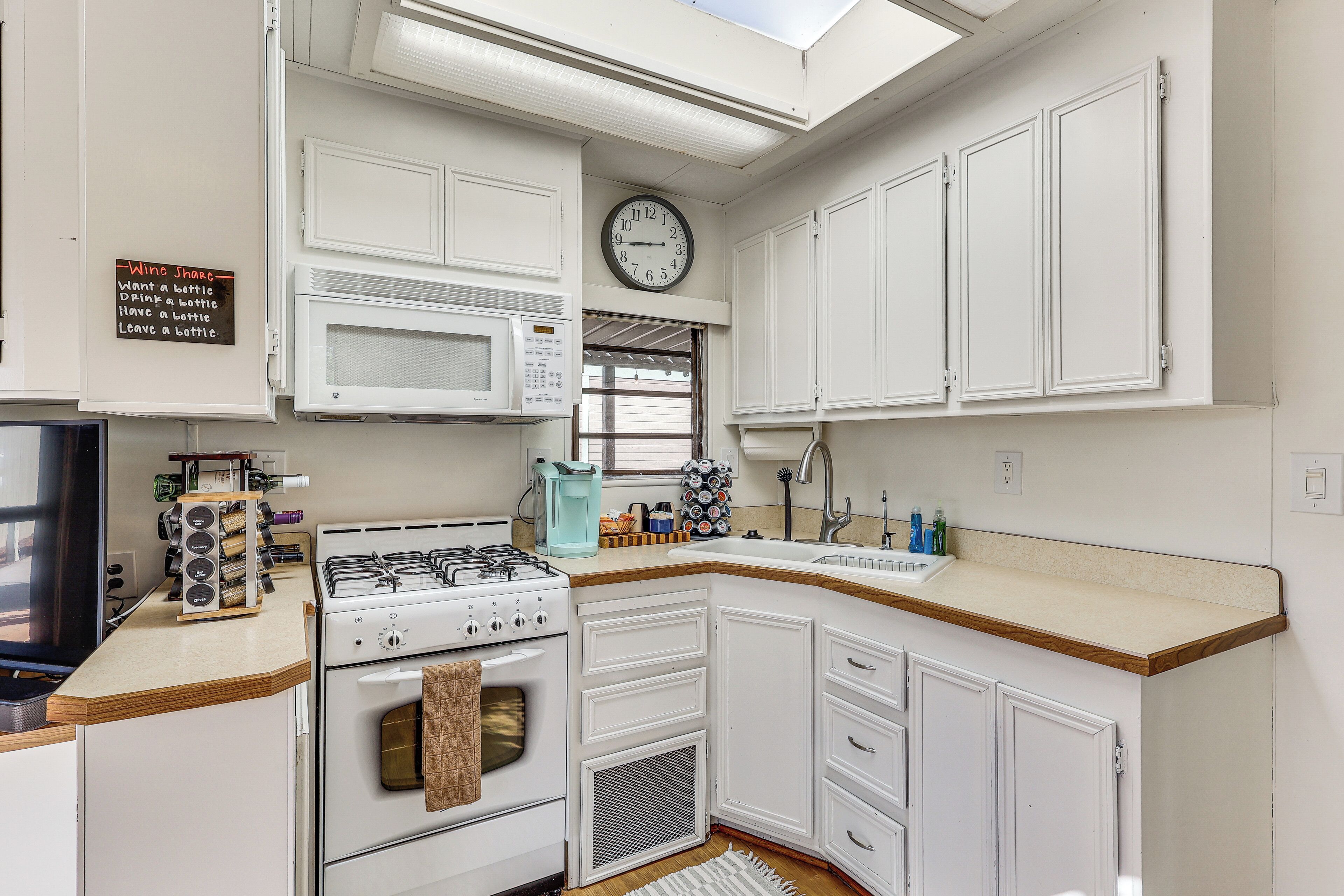 A kitchen with white cabinets, a stove, a microwave, and a clock on the wall.