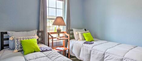 A bedroom with two beds, a window with curtains, a lamp, and a chair.