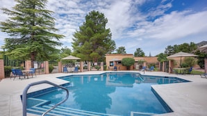 A rectangular outdoor swimming pool with a metal safety railing, surrounded by lounge chairs and umbrellas, with trees and a building in the background. - Sedona Condo w/ Pool, Hot Tub, & Pickleball! (Sedona)