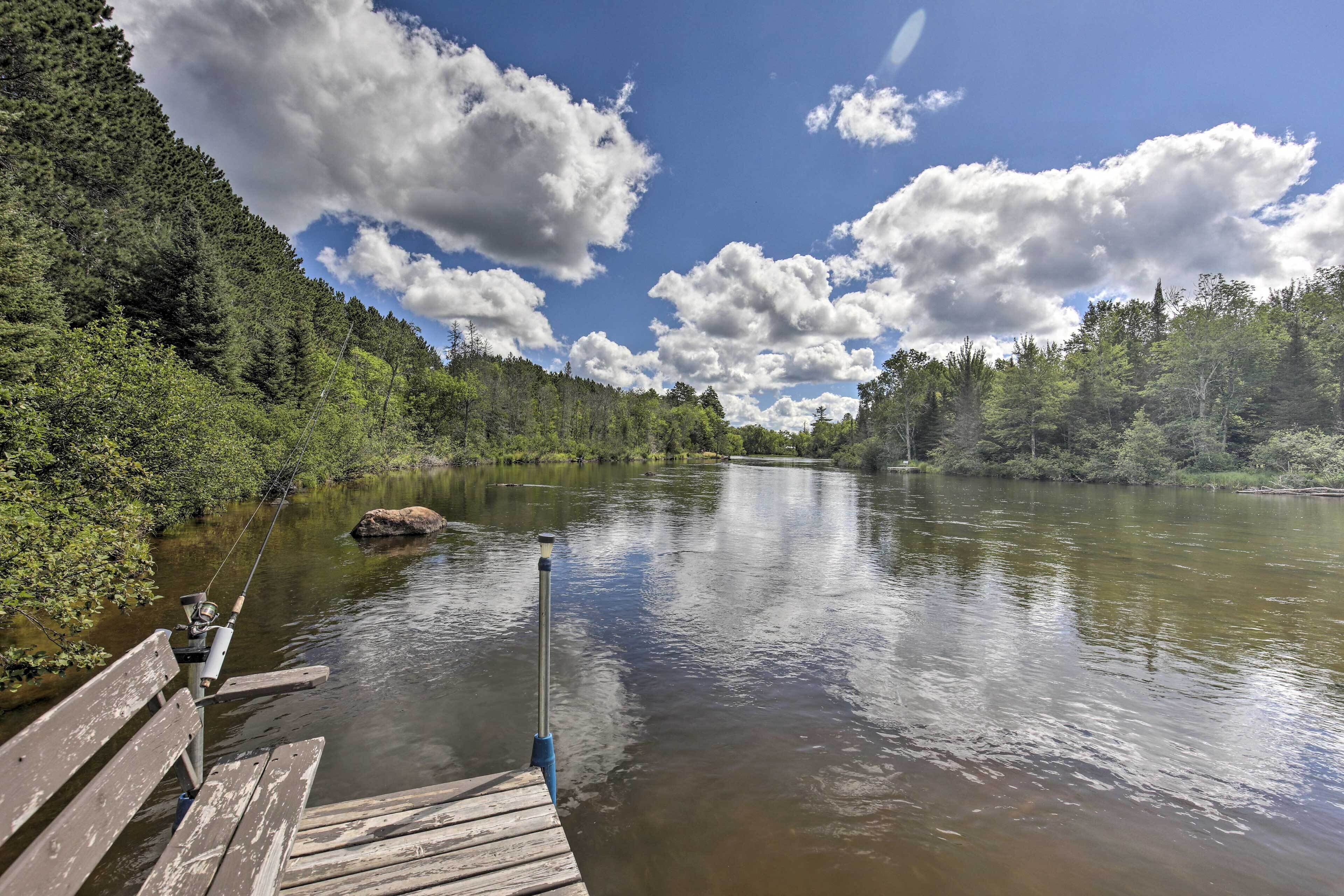 A wooden dock extending into a calm river surrounded by dense forest.