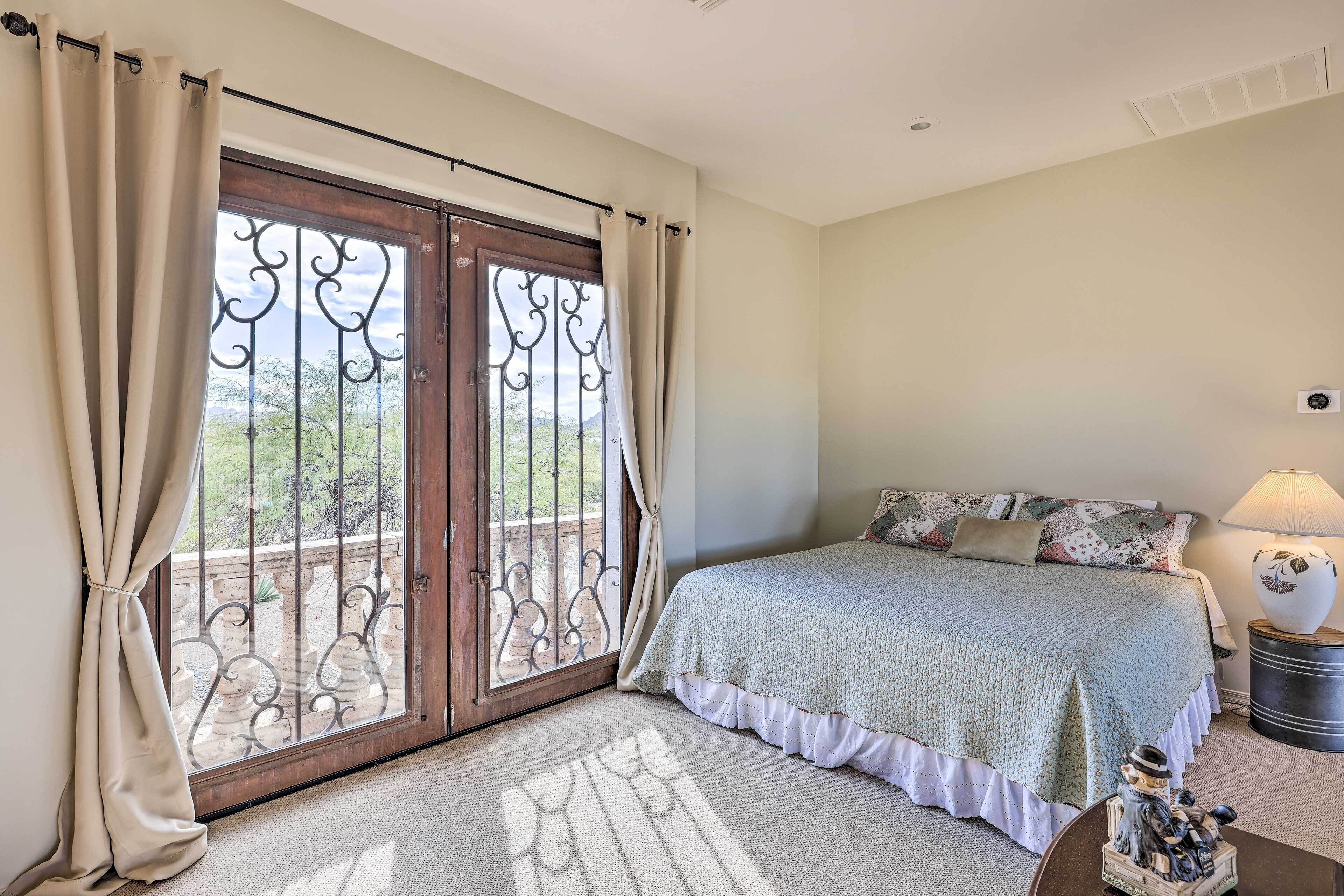 A bedroom with a bed, curtains, a nightstand, a lamp, and a view through a door with a metal gate.