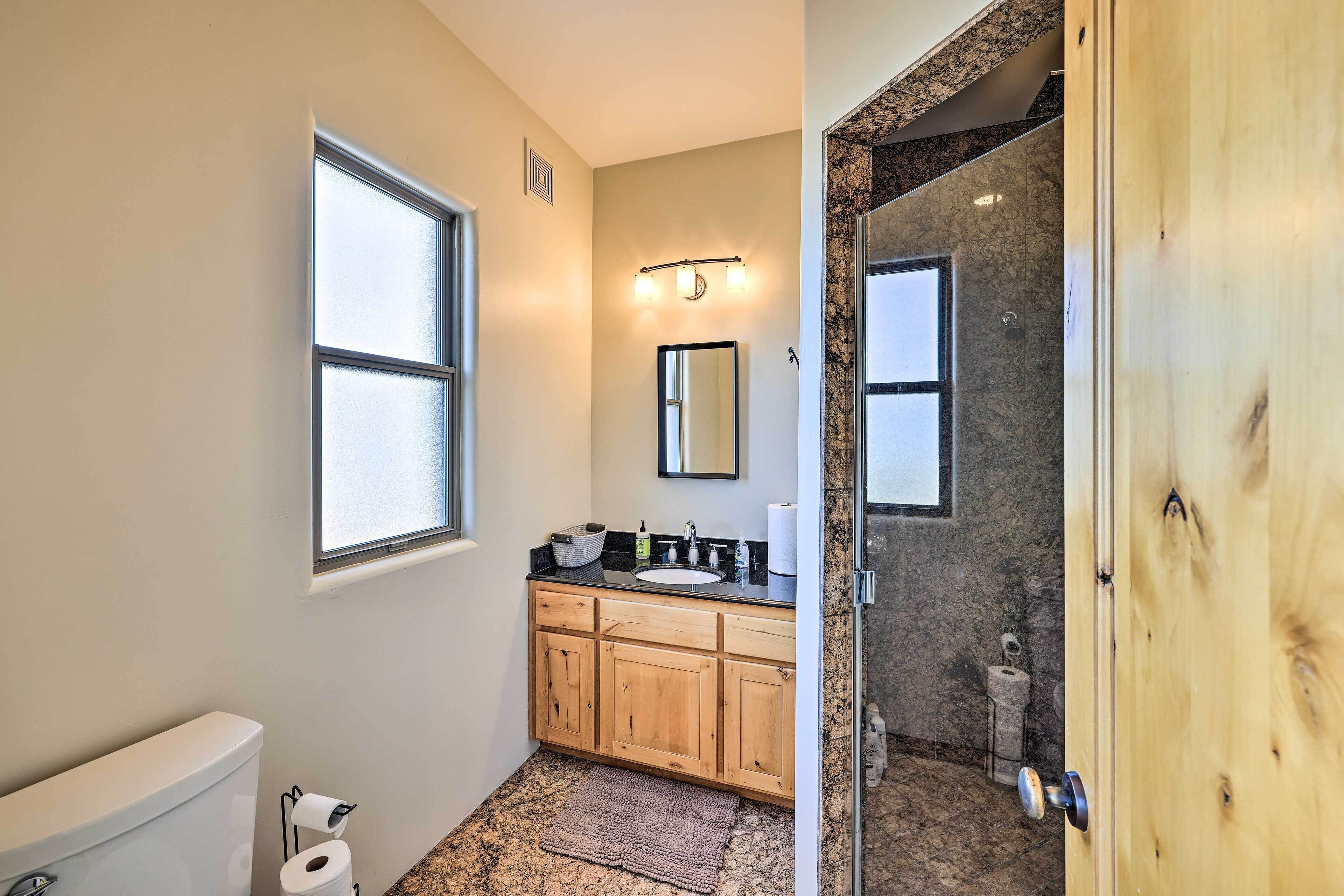 A bathroom with a toilet, sink, wooden cabinets, a mirror, and a shower area.