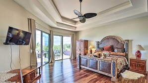 A spacious bedroom with a large bed, a ceiling fan, a television mounted on the wall, and a view of the outdoors through large sliding glass doors. - Backyard Oasis! Mtn-view Family Gem in Scottsdale (Scottsdale)