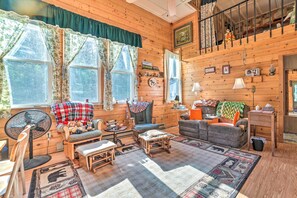 Een gezellig houten interieur met een slaapverdieping, een eethoek en een woonkamer, gemeubileerd met een bank, stoelen en een ventilator.