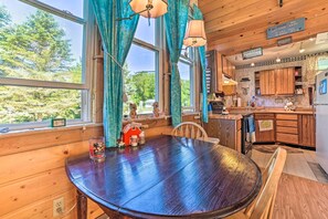 Un interior de madera con una mesa redonda, una zona de cocina y vistas al exterior a través de amplios ventanales.